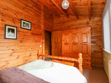 A bedroom with wooden walls a wooden wardrobe a wooden bed and two framed pictures at Bittern Lodge in Tattershall Lakes Country Park