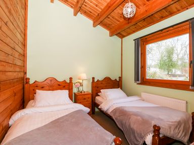 A bedroom with two single beds a nightstand with a lamp and flowers and a window showing trees at Bittern Lodge in Tattershall Lakes Country Park