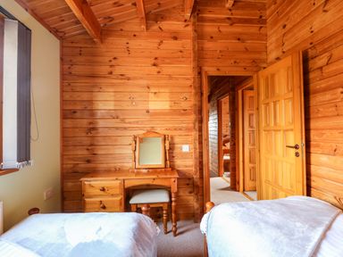 A bedroom with two single beds a wooden dressing table and an open door in a wooden cabin at Bittern Lodge in Tattershall Lakes Country Park