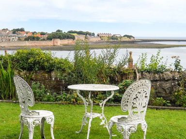 A white metal table and two chairs on grass with a stone wall and river view at The Lookout in Berwick-upon-Tweed