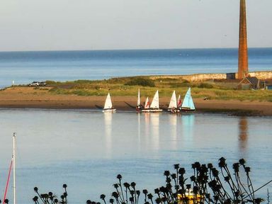 Small sailboats docked near a shoreline with a tall chimney and grassy area at The Lookout in Berwick-upon-Tweed