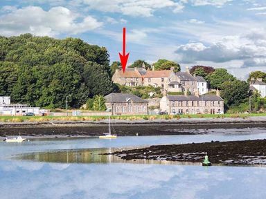 A body of water with boats and houses on a hillside with trees and a red arrow pointing to one house at The Lookout in Berwick-upon-Tweed