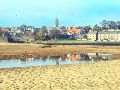 A sandy beach with a shallow water pool reflecting buildings and a church tower in the background at The Lookout in Berwick-upon-Tweed