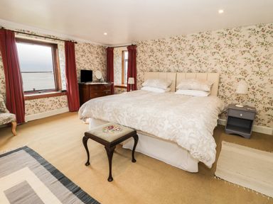 A bedroom with a large bed two windows a wooden chest of drawers and a small stool at The Lookout in Berwick-upon-Tweed