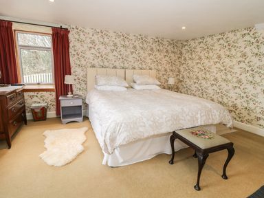 A bedroom with a double bed bedside tables chest of drawers window with red curtains and floral wallpaper at The Lookout in Berwick-upon-Tweed