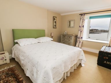 A bedroom with a bed with green headboard a dresser a window with a view and a trunk at The Lookout in Berwick-upon-Tweed
