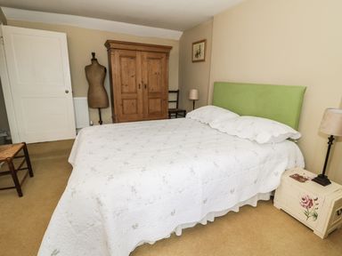 A bedroom with a bed with a green headboard a white quilt a wooden wardrobe two chairs two lamps and a painted bedside cabinet at The Lookout in Berwick-upon-Tweed