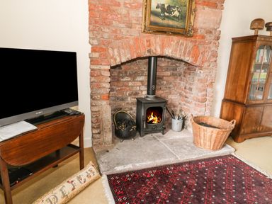 A room with a brick fireplace and wood-burning stove next to a television on a wooden table at The Lookout in Berwick-upon-Tweed