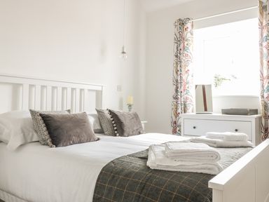 A bedroom with a white bed frame two gray pillows folded towels on the bed a white dresser next to a window with floral curtains at The Stable in Berkeley