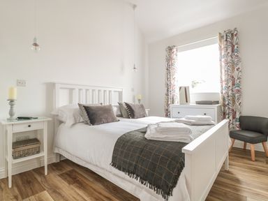 A bedroom with a white bed a side table candles a dresser with a mirror and patterned curtains at The Stable in Berkeley