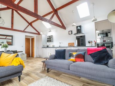 An open living room and kitchen with gray sofas and wooden ceiling beams at The Stable in Berkeley