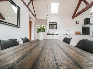 A kitchen with a wooden dining table and black chairs with white flowers in a vase at The Stable in Berkeley
