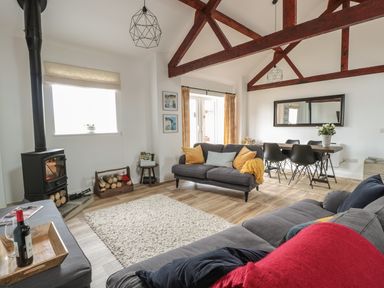 A living room with two sofas a wood burning stove a dining table and chairs and exposed wooden beams at The Stable in Berkeley