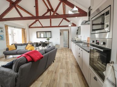 An open kitchen and living room with gray sofas wooden floor and exposed wooden beams at The Stable in Berkeley