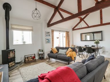 A living room with wooden beams on the ceiling two grey sofas and a dining table with black chairs at The Stable in Berkeley