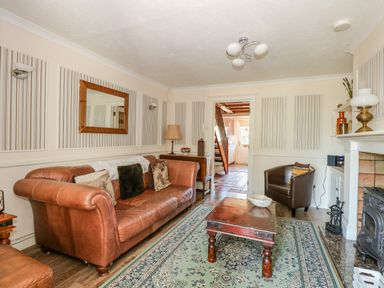 A living room with a leather sofa a wooden coffee table and a fireplace at Camerons Cottage in Swaffham