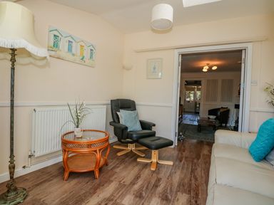 A sitting room with a glass top wicker table black armchair and a white sofa at Camerons Cottage in Swaffham