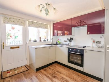 A kitchen with grey and purple cabinets a built in oven a sink below windows and a door with stained glass at Camerons Cottage in Swaffham