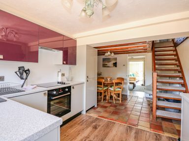 A kitchen with purple and beige cabinets a built-in oven and a dining table with chairs near stairs at Camerons Cottage in Swaffham