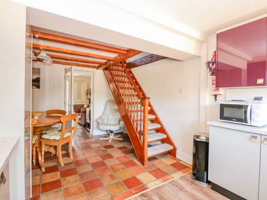 A kitchen and dining area with wooden stairs and a white armchair at Camerons Cottage in Swaffham