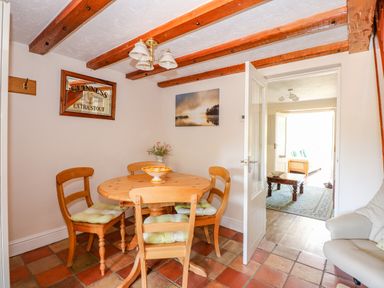A dining area with a round wooden table and four chairs with cushions a glass door leading to a living room at Camerons Cottage in Swaffham
