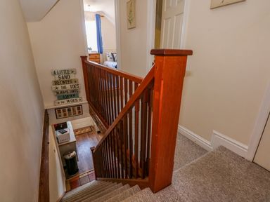 A stairway with wooden railing leading down to a kitchen area with a microwave and trash bin at Camerons Cottage in Swaffham