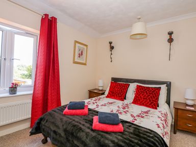 A bedroom with a double bed red curtains bedside tables and towels on the bed at Camerons Cottage in Swaffham