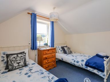 A bedroom with two single beds a wooden chest of drawers and a window with blue curtains at Camerons Cottage in Swaffham