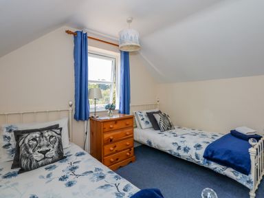 A bedroom with two single beds blue floral bedding wooden chest of drawers and blue curtains at Camerons Cottage in Swaffham