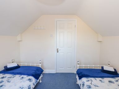 A bedroom with two beds covered in blue and white floral bedding facing a closed white door at Camerons Cottage in Swaffham
