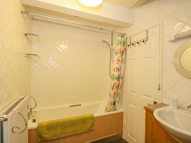 A bathroom with a bathtub and shower curtain next to a door and a sink with mirror at Camerons Cottage in Swaffham