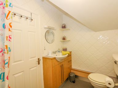 A bathroom with a white door a colorful shower curtain a sink with a wooden cabinet a round mirror and a toilet at Camerons Cottage in Swaffham