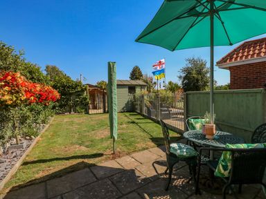 A garden with a patio table and chairs under an umbrella a shed and flags at Camerons Cottage in Swaffham