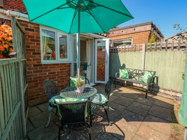 A small outdoor patio with a table and chairs under a large umbrella and a bench with cushions at Camerons Cottage in Swaffham