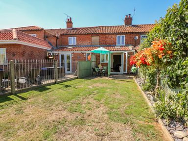A backyard with a patio table and umbrella a grass lawn and flower bushes at Camerons Cottage in Swaffham