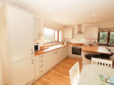 A kitchen with cream cabinets wooden countertops a dining table with chairs and bar stools at Bodneithior in Llanerchymedd