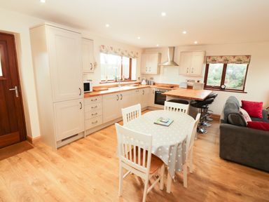 A kitchen and dining area with white cabinets wooden countertops a dining table with four chairs and a grey sofa at Bodneithior in Llanerchymedd