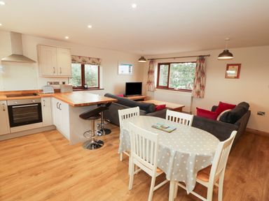 An open plan kitchen living and dining area with wooden floors and white furniture at Bodneithior in Llanerchymedd