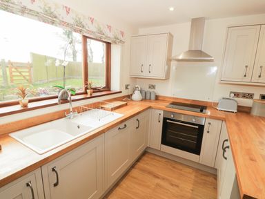 A kitchen with a sink under a window and a stovetop with an oven and wooden countertops at Bodneithior in Llanerchymedd