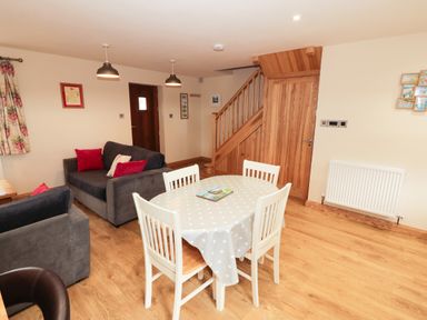 A living room with a dining table with four chairs and wooden staircase at Bodneithior in Llanerchymedd