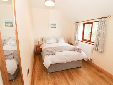 A bedroom with a bed two bedside tables lamps a window with curtains and a wall mirror at Bodneithior in Llanerchymedd