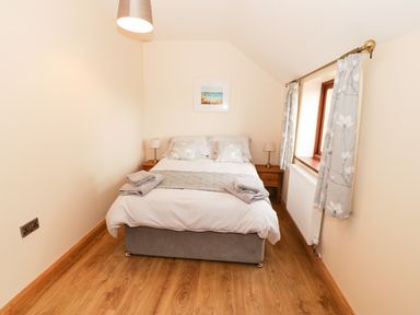 A small bedroom with a double bed two bedside tables with lamps a window with floral curtains and wooden flooring at Bodneithior in Llanerchymedd