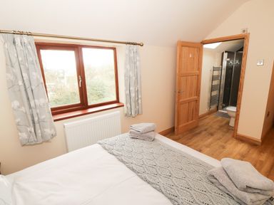 A bedroom with a bed and folded towels near a window and an open door showing a bathroom at Bodneithior Llanerchymedd
