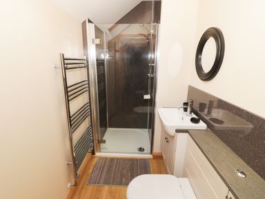A bathroom with a shower enclosure a sink with countertop a round mirror a towel rack and a toilet at Bodneithior Llanerchymedd