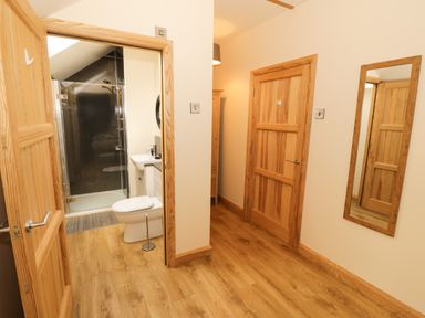 A hallway with wooden doors a full-length mirror and a bathroom with a shower at Bodneithior in Llanerchymedd