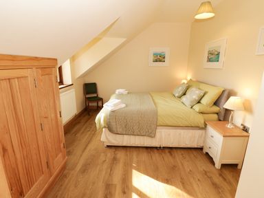 A bedroom with a bed side table a chair a wooden wardrobe and framed pictures on the walls at Bodneithior in Llanerchymedd