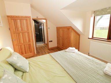 A bedroom with a bed towels wooden doors built in storage and a window at Bodneithior in Llanerchymedd