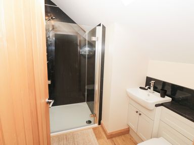 A bathroom with a glass shower enclosure and a white sink with black countertop at Bodneithior in Llanerchymedd