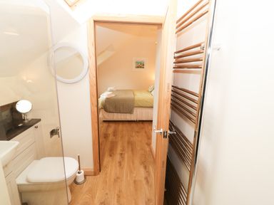 A bathroom with a toilet sink and mirror leading to a bedroom with a made bed and wooden floor at Bodneithior in Llanerchymedd