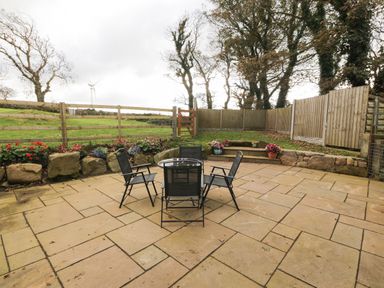 An outdoor patio with four black chairs around a glass table surrounded by stone walls and fencing at Bodneithior in Llanerchymedd